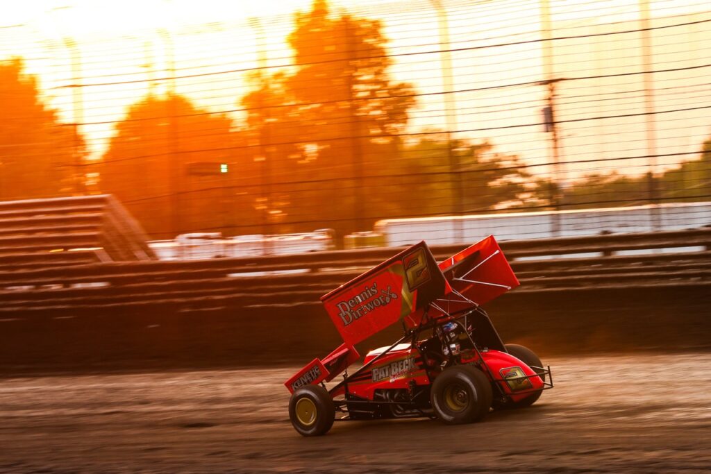 ASCS Frontier Region driver Kelly Miller driving his Sprint Car around a racetrack beneath a sunset sky